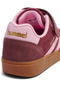 Bordeauxroter Wildleder-Sneaker mit rosa Akzenten, einem strukturierten Design und einem Klettverschluss. Goldenes Logo an der Ferse und Laufsohle aus Kautschuk.