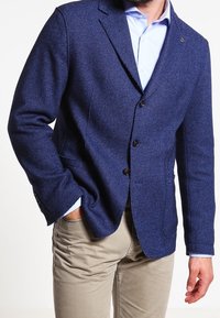 Námorněmodrý blazer s texturovanou tkaninou, jednoradový design, tři knoflíky a klopový límec, spárovaný s světle modrou košilí.