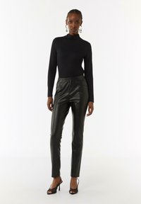 Zwarte coltrui gecombineerd met hoge, strakke zwarte leren broeken. Accessoires zijn grote, patronen oorbellen en zwarte, strappy hakken.