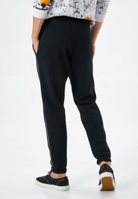 Svarta joggerbyxor med elastisk midja, sidofickor och smalnande avslut, kombinerat med svarta sneakers och en sweatshirts med texturmönster.