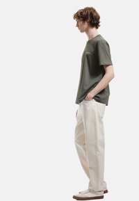 Olivgrünes kurzärmliges T-Shirt kombiniert mit cremefarbenen weit geschnittenen Hosen. Das Shirt hat ein schlichtes Design und eine lockere Passform, die den Komfort betont.