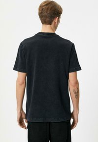 Camiseta de algodón negra con un ajuste relajado, cuello redondo y mangas cortas, que presenta una textura deslavada y un dobladillo recto.