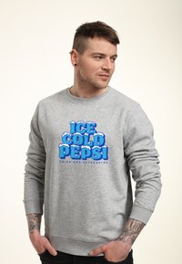Šedá mikina vyrobená z bavlněné směsi, s modrým sněhovým textovým grafickým prvkem, který říká "ICE COLD PEPSI" a pod ním je text "CRISP AND REFRESHING".