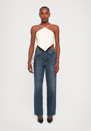 Witte, asymmetrische crop top met dunne bandjes, gecombineerd met hoge taille, rechte donkerdenim jeans en zwarte spitse hakken.