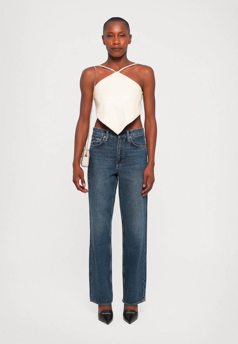 Witte, asymmetrische crop top met dunne bandjes, gecombineerd met hoge taille, rechte donkerdenim jeans en zwarte spitse hakken.