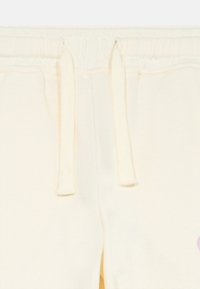 Nahaufnahme des Bunds einer cremefarbenen Sweatpants mit Kordeln und teilweisen Taschen auf einem hellen Hintergrund.