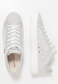 Ljust grå sneakers med ett strukturerat tygöverdrag och släta syntetiska detaljer. Har vita snören och en vit gummisula.