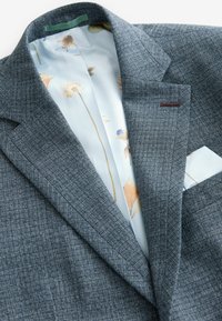 Szary, teksturowany blazer z wzorzystą podszewką z kwiatowymi motywami w delikatnych kolorach. Zawiera dopasowany detal w postaci chusteczki w kieszeni.