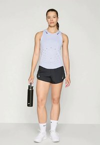 Svijetloplavi bezrukavni sportski top s perforiranim dizajnom, uparen s crnim kratkim hlačama, držeći crnu bocu s vodom, nosi bijele tenisice.