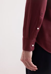 Camicia a maniche lunghe color bordeaux con tessuto lavorato, polsini abbottonati e un discreto dettaglio del logo sulla manica.