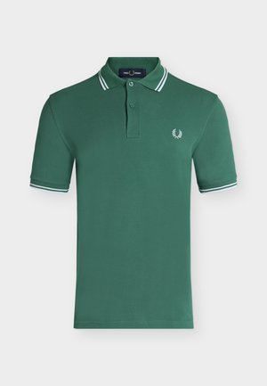 Polo vert à manches courtes avec doubles bandes blanches sur le col et les poignets, patte à deux boutons, et petit logo de laurier blanc sur la poitrine gauche.