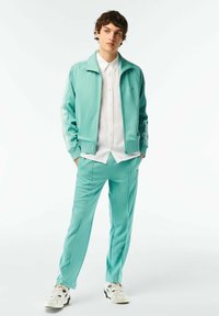 Completo tuta di un azzurro chiaro realizzato in un materiale morbido, con giacca con zip e strisce laterali abbinata a pantaloni slim-fit, abbinati a sneakers bianche.