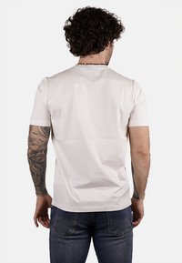 T-shirt leggero a maniche corte, di colore crema, con collo tondo. Texture liscia e design minimalista, mostrato di spalle con jeans blu.