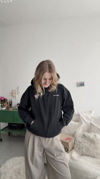 Svart hoodie med framficka och en liten grafik på vänster sida. Kombinerad med beige vida byxor. Avslappnad, bekväm passform.
