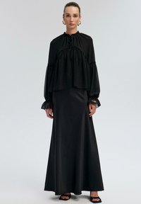 Black layered blouse with elastic neck and sleeves paired with a satin black maxi skirt. Smooth texture, long sleeves, and minimal detailing.