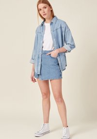 Chaqueta de mezclilla azul clara con un corte relajado, combinada con una falda mini de mezclilla a juego y zapatillas blancas de caña alta. Camiseta blanca lisa debajo.