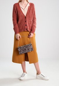 Pletený cardigan v rezavé barvě s výstřihem do V a zapínáním na knoflíky, doplněný hořčicovou zavinovací sukní a psaníčkem s motivem zvířecí kůže. Bílé tenisky.