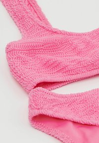 Růžový bikiny top s texturovaným, volánkovým designem s nepravidelnými vlnkami. Popruhy jsou také volánkové, což celkově vytváří jednotný estetický dojem.