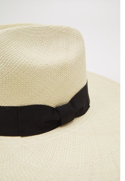 Chapeau en paille à large bord de couleur beige clair, avec un ruban noir enroulé autour de la base, présentant un motif tissé texturé.