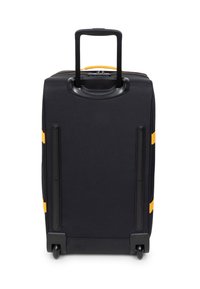 Musta pyörillä varustettu matkalaukku, jossa on sisään vedettävä kahva, keltaisia yksityiskohtia, sileä pinta ja pohjassa suojaavat metalliosat.