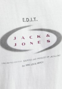 Hvid T-shirt med grå og maroon grafisk tekst, der står "E.D.I.T. Jack & Jones," med cirkulære detaljer og produktinformation nedenfor.
