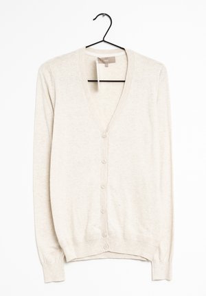 Hellbeiger Strickjacke mit Knöpfen, langen Ärmeln und gerippten Bündchen, die an einem schwarzen Kleiderbügel vor weißem Hintergrund hängt.