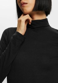 Svart polotröja med långa ärmar, gjord av ett slätt tyg. Har en hög krage och enkel design, utan synliga mönster eller detaljer.