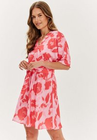 Šaty s krátkým rukávem v růžovo-červeném tie-dye vzoru, s výstřihem do V a nastavitelným páskem v pase, vyrobené z lehkého materiálu.