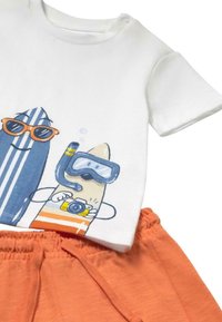 Camiseta blanca de algodón con gráfico de tabla de surf en azul y naranja, que presenta un diseño de esnórquel. Combinada con pantalones cortos naranjas texturizados.
