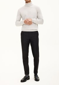 Hellgrauer Rollkragenpullover, taillierte Passform, gerippte Bündchen. Kombiniert mit schwarzen, maßgeschneiderten Hosen, leicht zulaufend, getragen mit schwarzen Loafers.