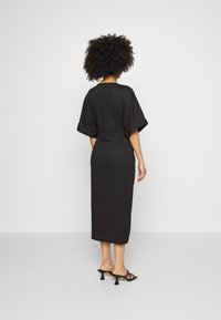 Svart, knälång klänning med korta, breda ärmar och figursydd midja. Slät tyg utan mönster; modellen stylad med svarta klacksandaler.