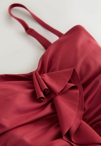 Sarkana satīna kleita ar plānām lencēm un uzliesmojošu volānu detaļu. Gluda tekstūra ar plūstošu dizainu un elegantu kritumu.