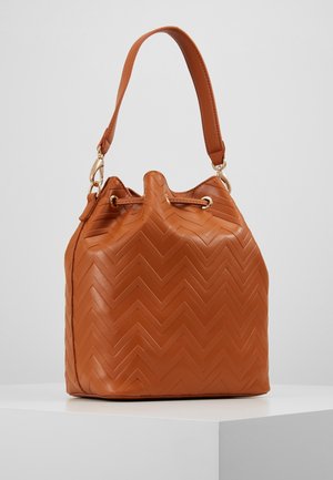 Hnědá kožená kabelka ve tvaru kbelíku se vzorem cik-cak prošívání, zlatými očeky a jedním horním úchopem na bílém povrchu.