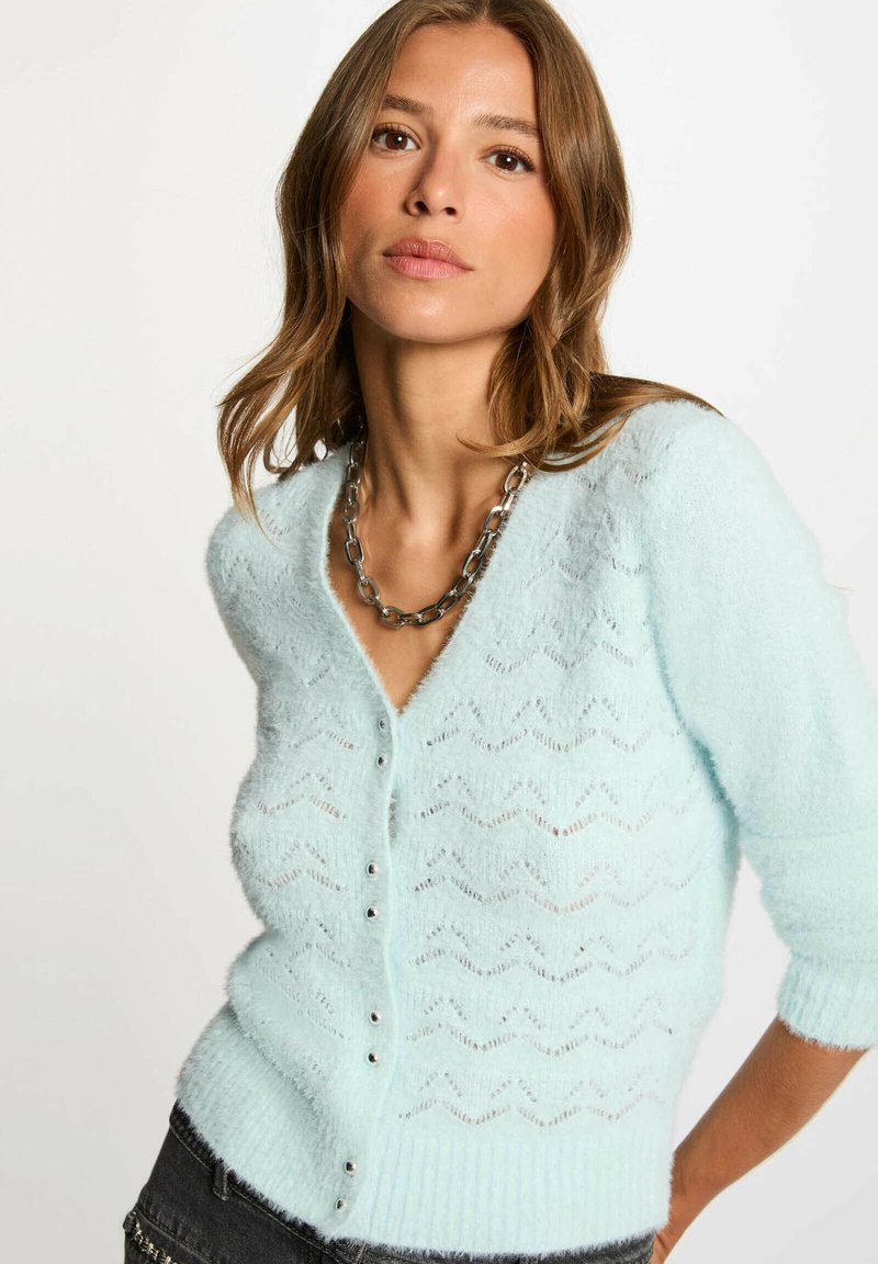 Cardigan azzurro chiaro con motivo a zigzag, realizzato in materiale morbido e soffice. Ha scollatura a V, chiusura con bottoni e maniche a tre quarti.