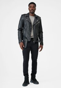 Zwarte leren motorjas met ritszakken, grijze crewneck trui, slim zwarte broek en zwarte veterschoenen.
