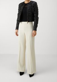 Černá kožená bunda s řasením a kulatým výstřihem, kombinovaná s krémovými kalhotami s vysokým pasem a širokými nohavicemi a černými lodičkami se špičatou špičkou.