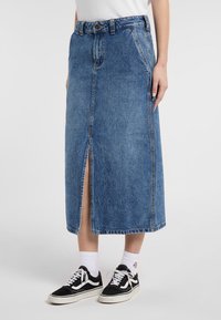 Vaaleansininen denim-mittapituinen hame, jossa on edessä halkio, muotoiltu vyötärö ja näkyvät ompeleet. Päällä mustat lenkkarit ja valkoiset sukat.