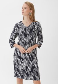 Knielanges Kleid in Marineblau mit einem weißen abstrakten Muster. Verfügt über einen V-Ausschnitt und drei Viertelärmel mit einer lässigen Passform. Glattes Material.