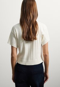 Top a maniche corte in maglia a coste bianco crema con orlo corto, caratterizzato da un ampio scollo e sottili contrasti di texture.