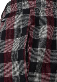 Tejido de franela a cuadros en negro, rojo y gris con un tejido texturizado. Presenta un diseño holgado y una cintura elástica.