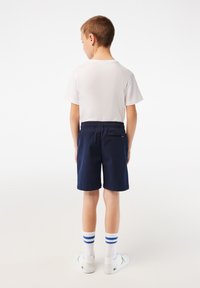 Pantaloni corti blu navy con cintura elastica e tasca posteriore, abbinati a una maglietta bianca e calzini bianchi con righe blu.