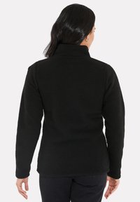 Veste en polaire noire avec un col montant et une surface texturée. Elle possède des manches longues et un ourlet droit, conçue pour offrir chaleur et confort.