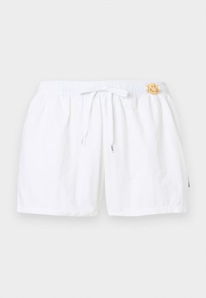 Shorts à taille élastique blanche avec cordon de serrage et petite épingle dorée en forme de visage souriant sur le côté droit, près de la taille.