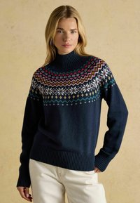 Marineblauer Pullover mit hohem, geripptem Kragen und buntem, geometrischem Passe-Muster mit weißen Schneeflocken und Akzenten in Pink, Grün und Gelb.