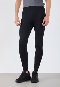 Fekete, rugalmas anyagból készült sportleggings, magas derékkal és sima textúrával, fekete sportcipővel viselve.