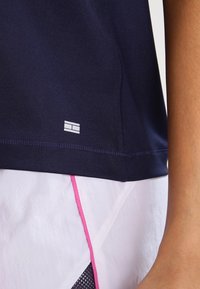 Navy blue, short-sleeved athletic shirt with stitch detail and a small white logo on the hem; paired with white shorts featuring pink accents.