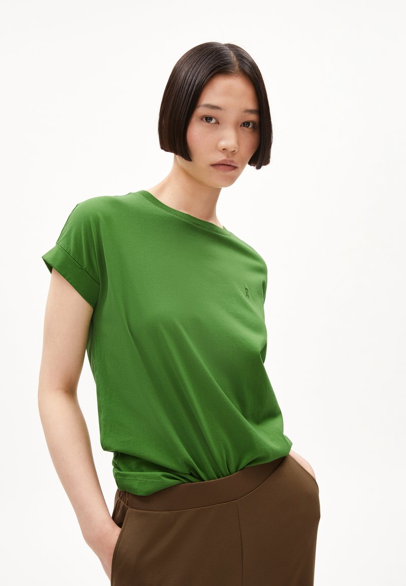 Camiseta verde de manga corta en tela suave, con un corte holgado y mangas enrolladas. Detalle sutil del logo en el área del pecho.