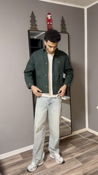 Giacca verde corta con bottoni metallici, indossata sopra una camicia bianca, abbinata a jeans azzurri e sneakers bianche. Specchio e decorazioni visibili.
