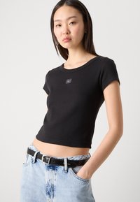 Black cropped t-shirt with short sleeves, ribbed texture, round neckline, and logo detail on the front, paired with high-waisted denim shorts.