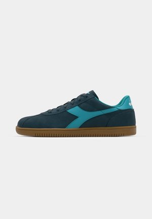Zapatillas de ante azul oscuro con acentos en azul claro, puntera redondeada, cordones en la parte frontal y suela de goma. Diseño minimalista con una textura suave.